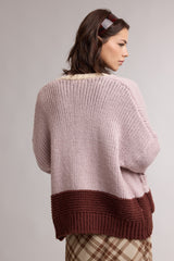 woman wearing a soft pink oversized knit sweater with a brown hem and checkered skirt, seen from the back