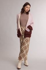 woman wearing a beige ribbed turtleneck, oversized pink and brown cardigan, and plaid wide-leg pants with cream ankle boots