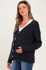 woman wearing a dark navy maternity cardigan with buttons, gently holding her baby bump, paired with a white top and jeans
