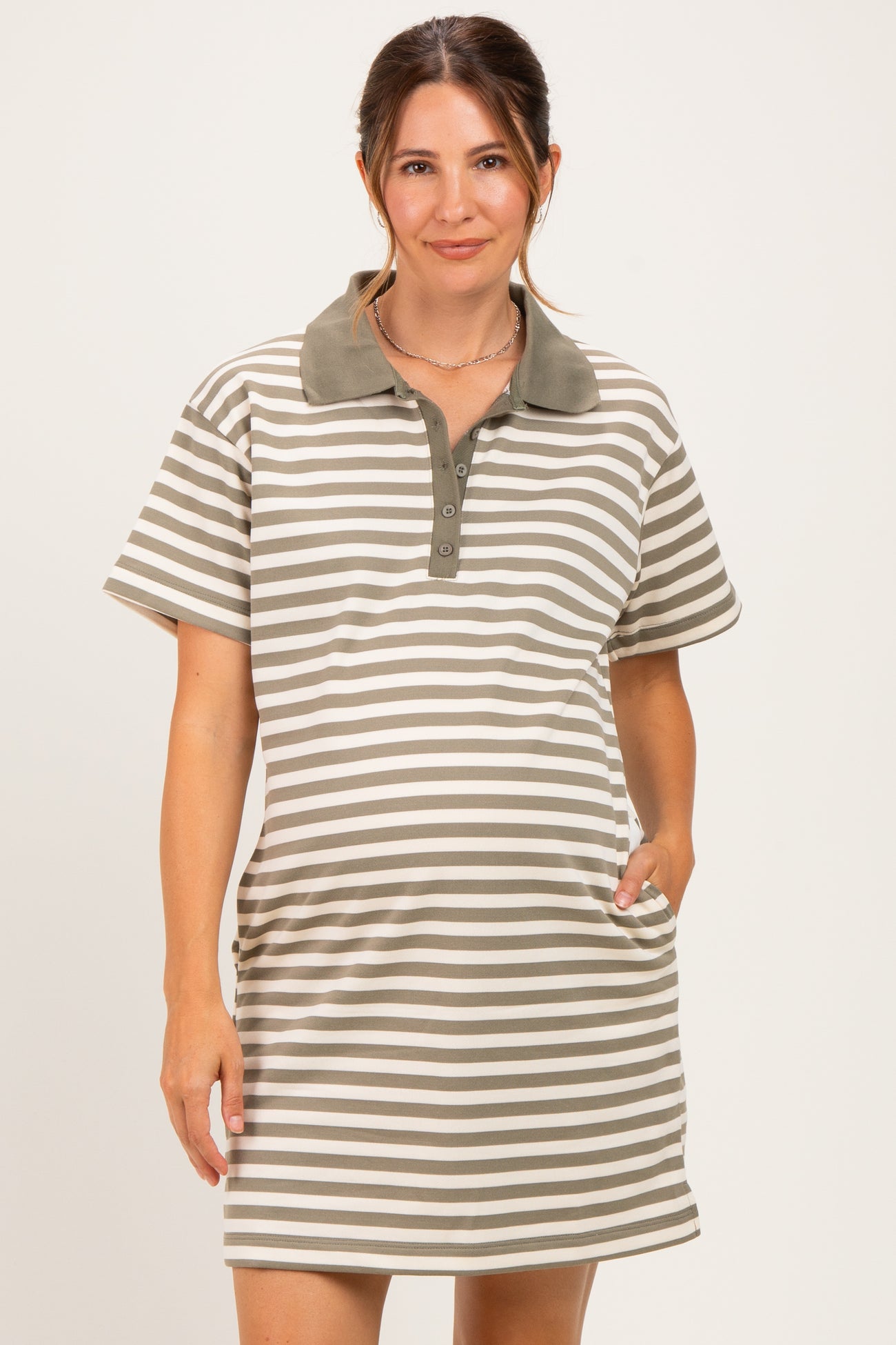 woman wearing a striped olive green maternity polo dress with a collar and pockets, showing a baby bump