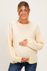 woman wearing a yellow and white striped maternity sweater and holding her baby bump