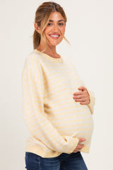 woman wearing a yellow and white striped maternity sweater and holding her baby bump