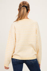 woman wearing a soft yellow striped oversized maternity sweater, seen from the back, styled with dark jeans