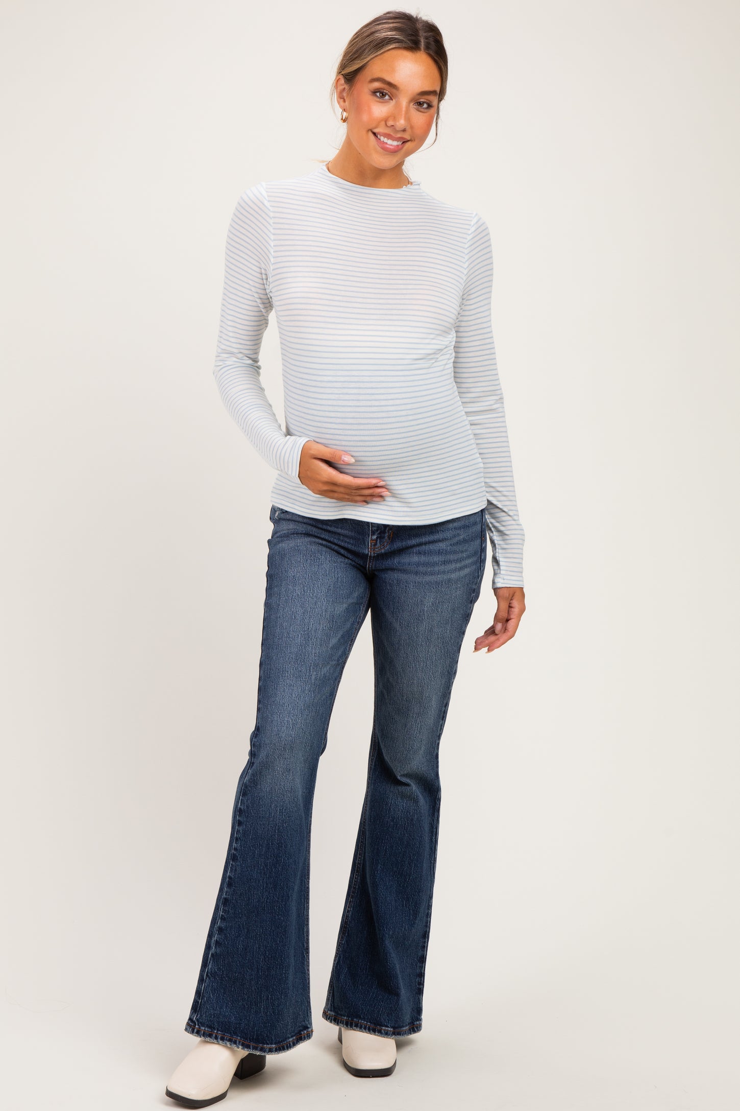 woman wearing a light blue and white striped long sleeve maternity top and holding her baby bump, paired with flared jeans