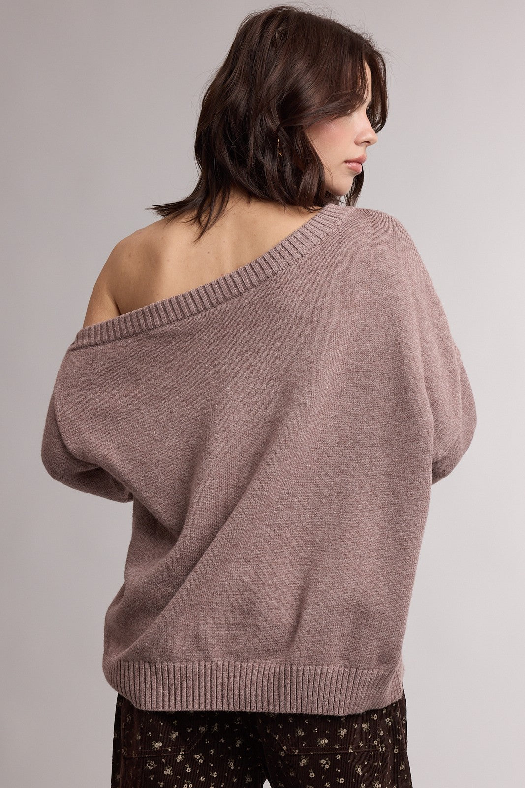 woman wearing a cozy mauve oversized sweater with an off-shoulder design and ribbed hem, seen from the back