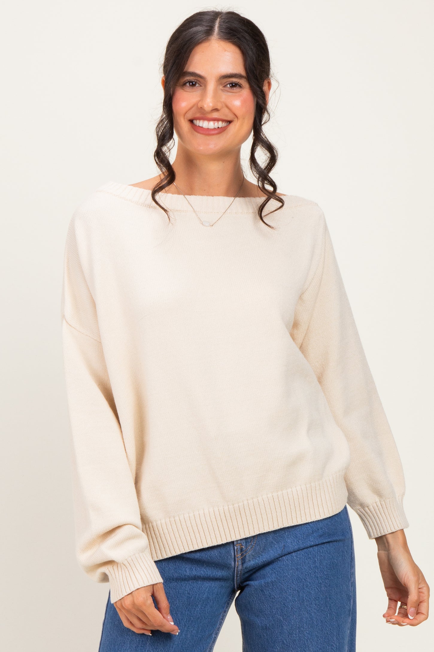 woman wearing a cream oversized sweater with a boat neck and balloon sleeves, smiling at the camera