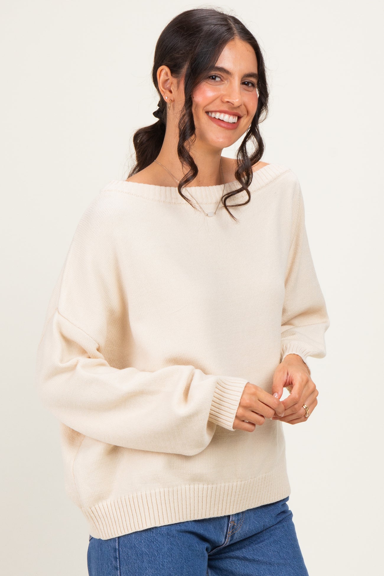 woman wearing a light beige oversized sweater with wide neckline and balloon sleeves paired with blue jeans