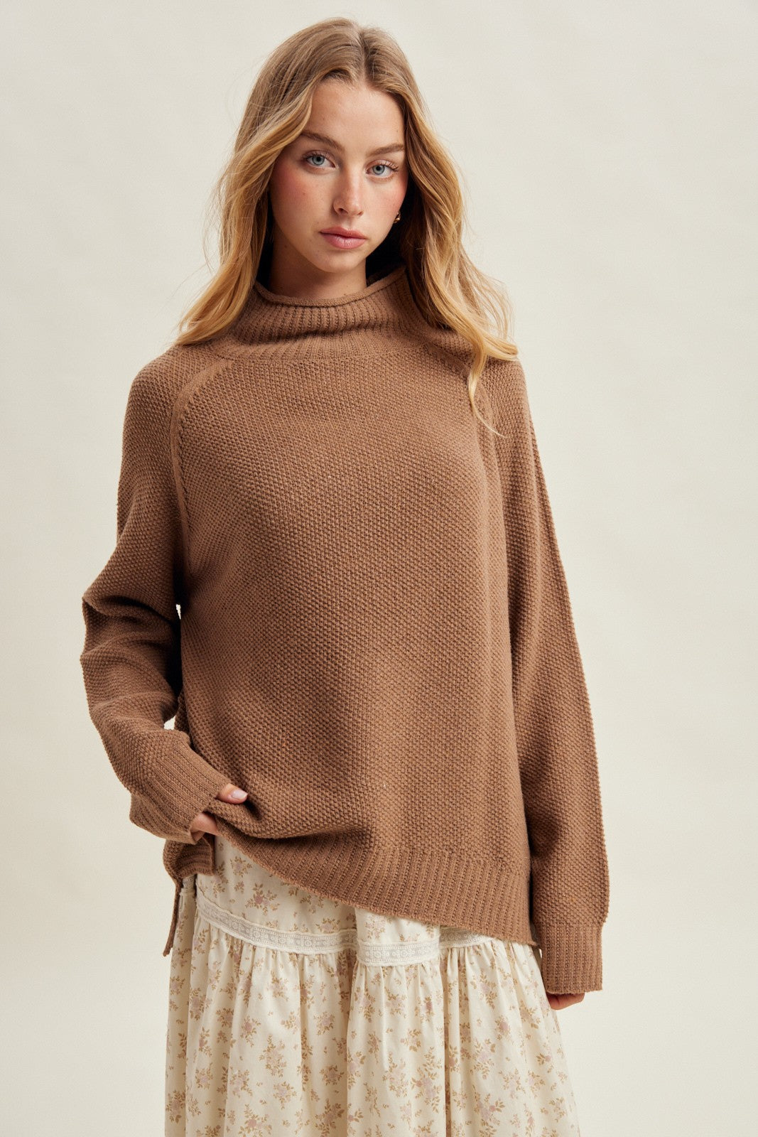 woman wearing a brown knit sweater with a high neckline paired with a floral print skirt