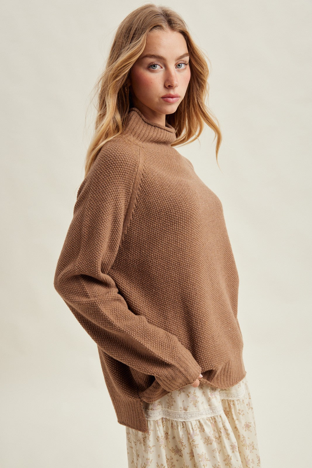woman wearing a brown oversized turtleneck sweater paired with a floral print skirt