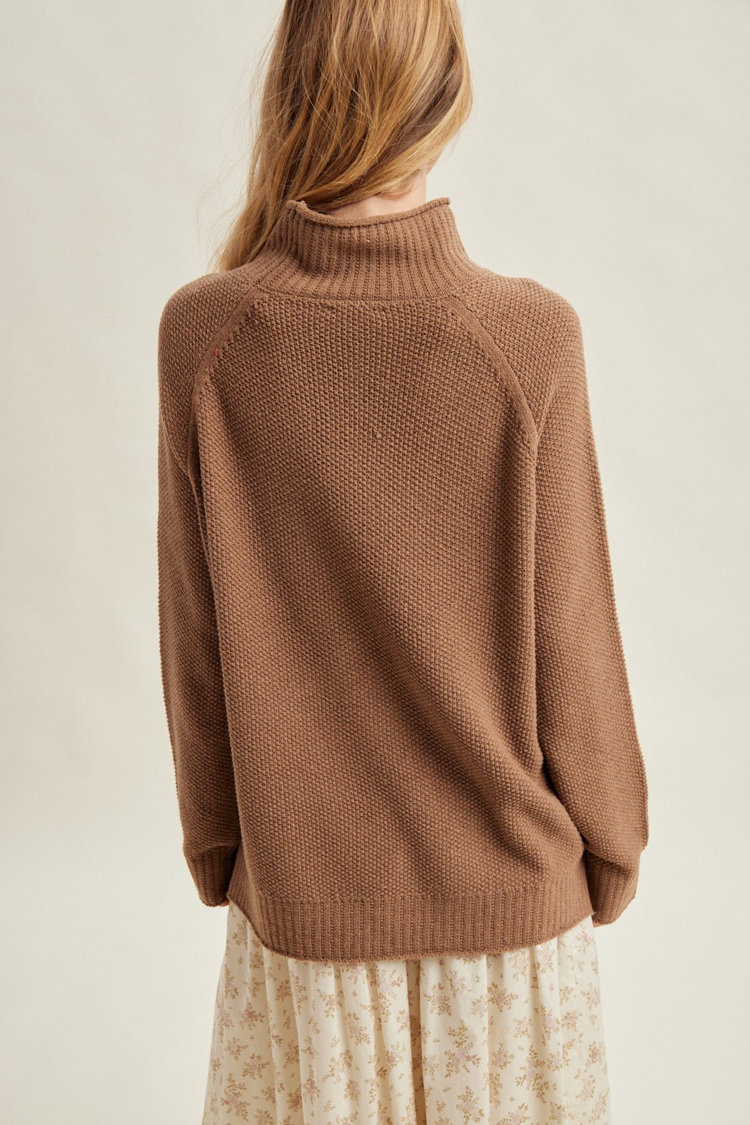woman wearing a brown knit sweater with a high collar, seen from the back over a floral dress