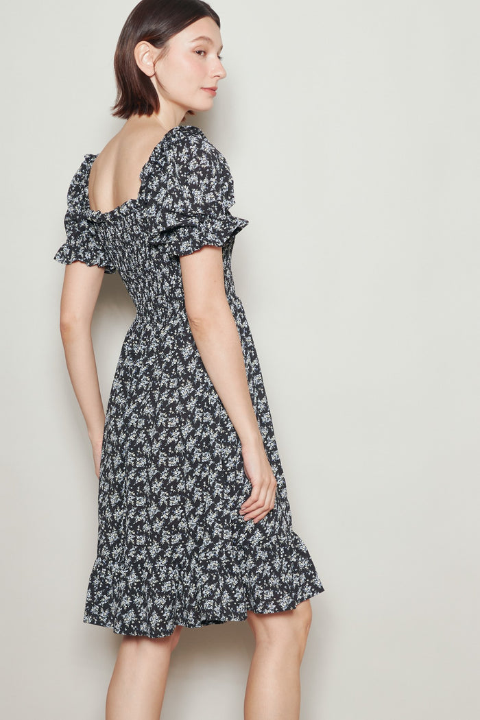 woman wearing a black floral puff sleeve dress with a ruffled hem and a square neckline