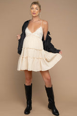 woman wearing a cream maternity dress with tiered ruffles and a v-neck, styled with a black jacket and knee-high boots