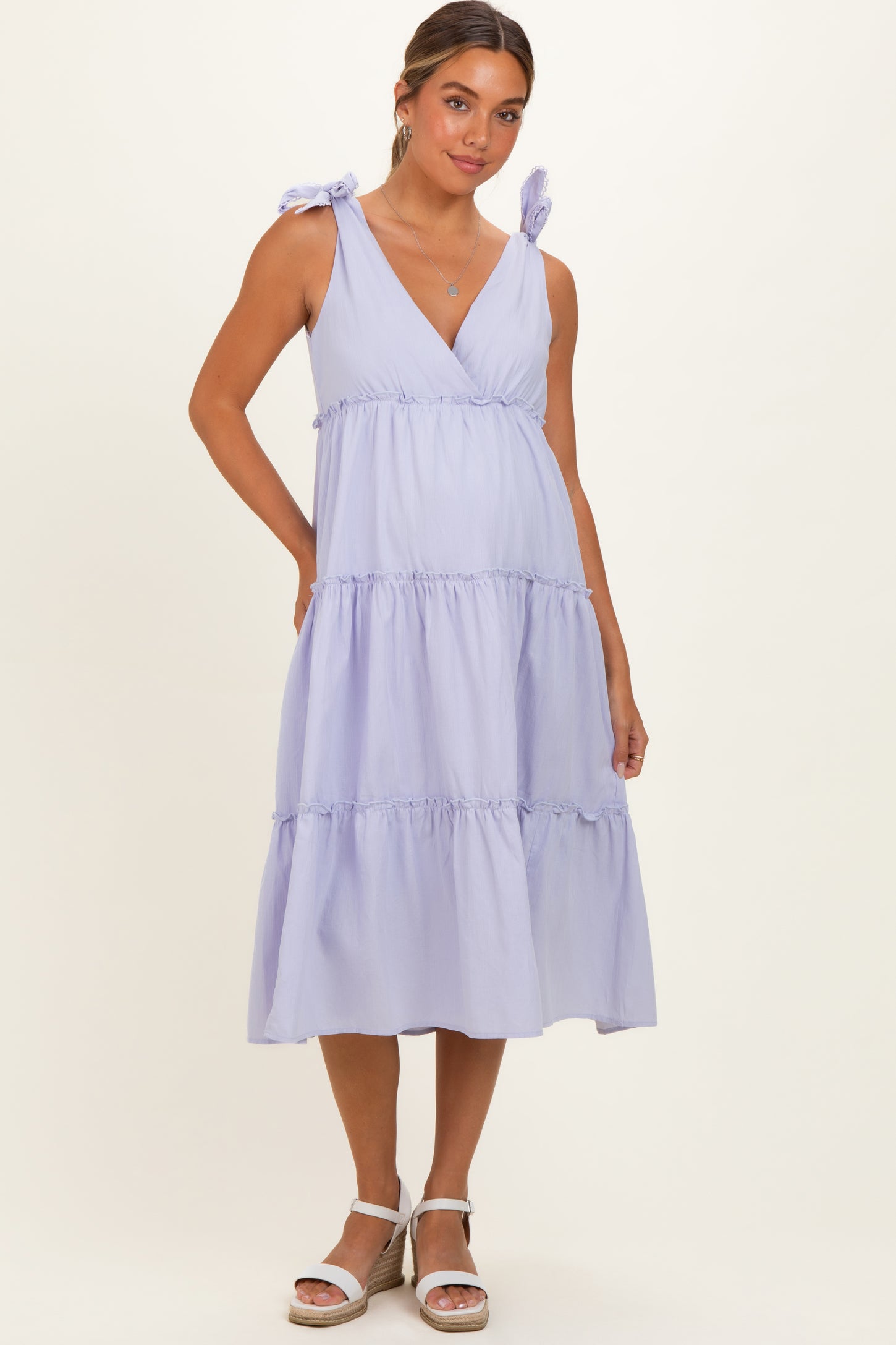 woman wearing a lavender maternity dress with tie shoulder straps and tiered ruffle details, showcasing her baby bump