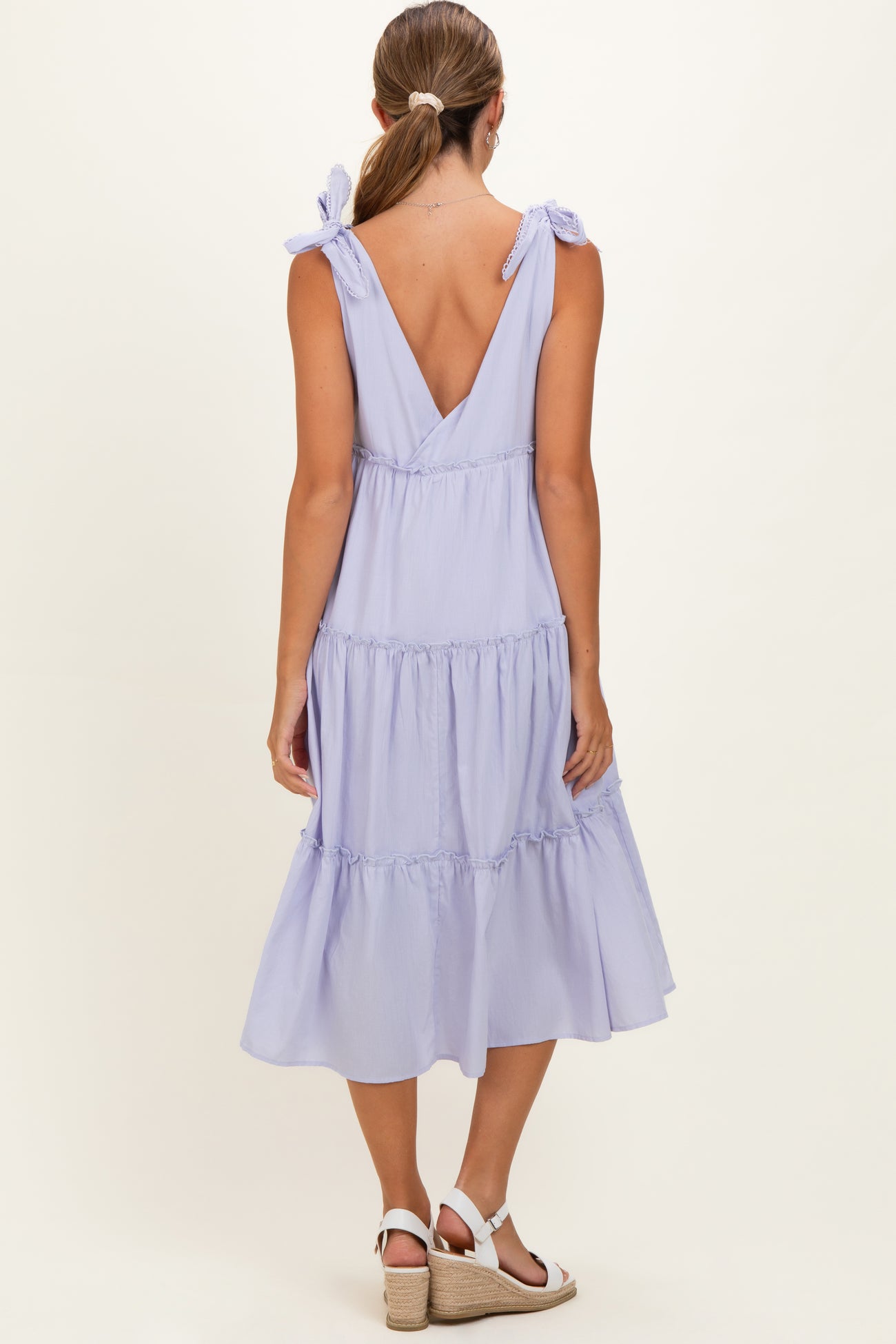 woman wearing a light purple maternity dress with tie straps and a tiered skirt, showing the back view