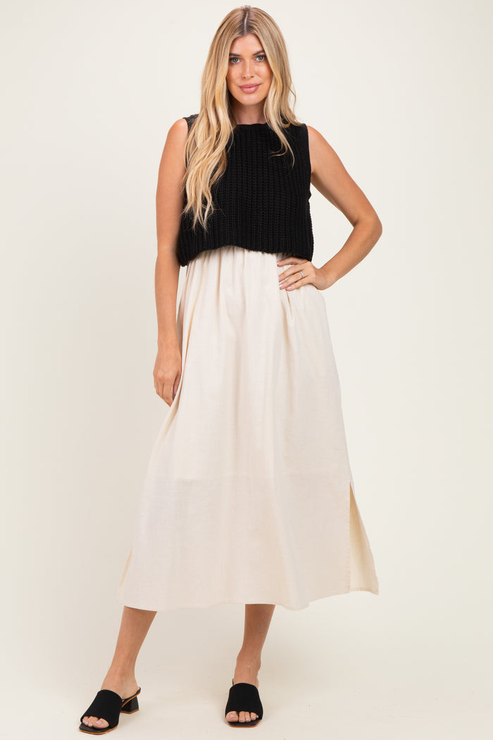 woman wearing a black knitted crop top over a cream maxi dress with side slits and black slide sandals