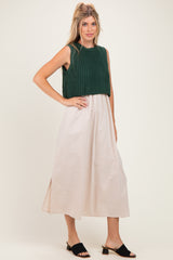 woman wearing a dark green knitted crop top and a light beige maxi skirt, standing in open-toe black mules