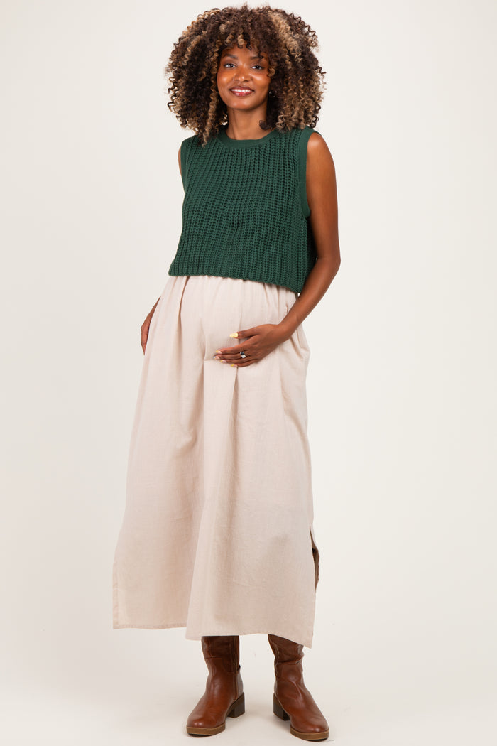 woman wearing a dark green knitted crop top and a light beige maxi skirt, showcasing her baby bump in maternity wear