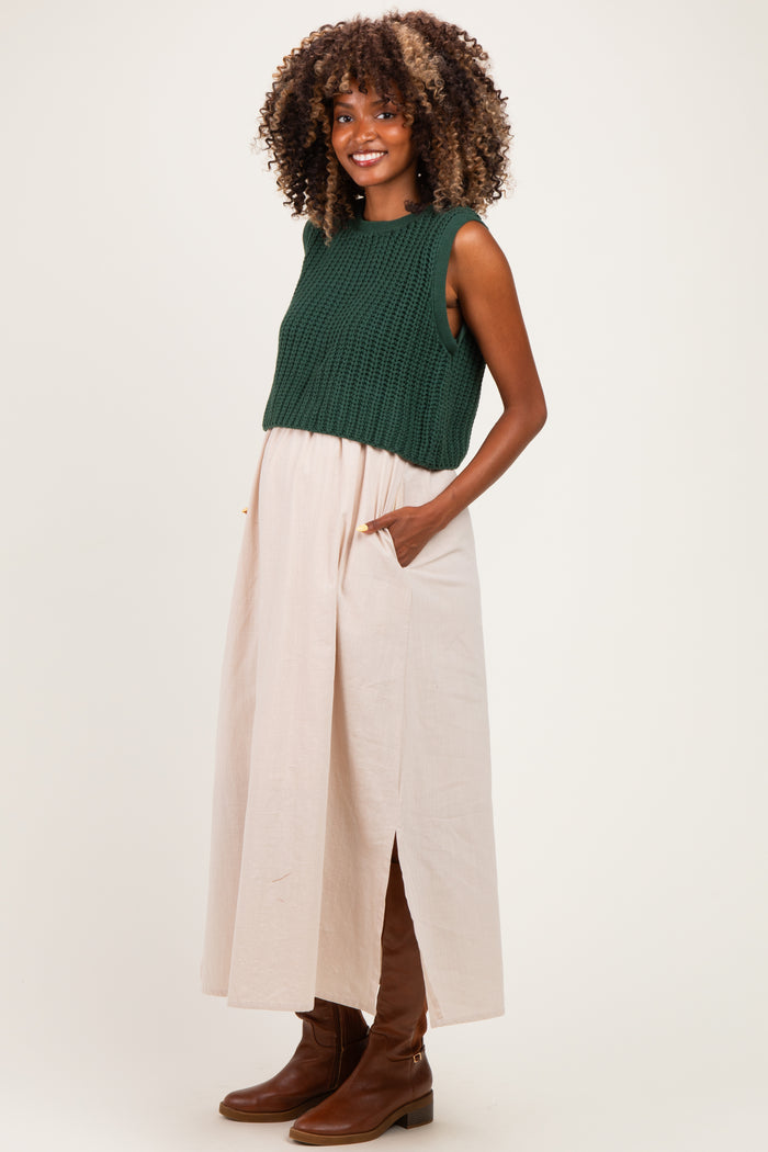 woman wearing a dark green knitted crop top and a light pink maxi skirt with pockets, showcasing her baby bump