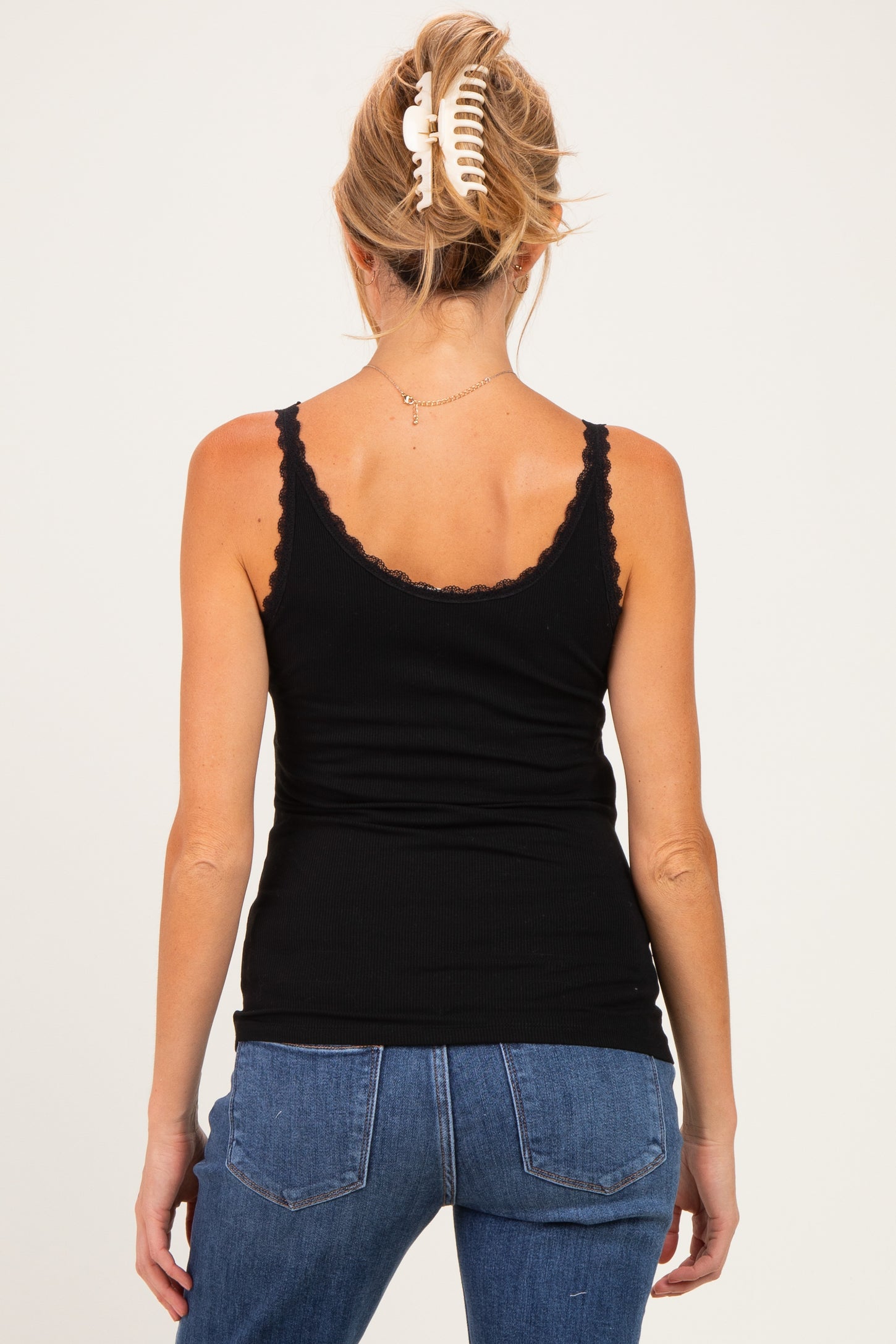 woman wearing a black maternity tank top with scalloped edges, showing her back and styled with blue jeans