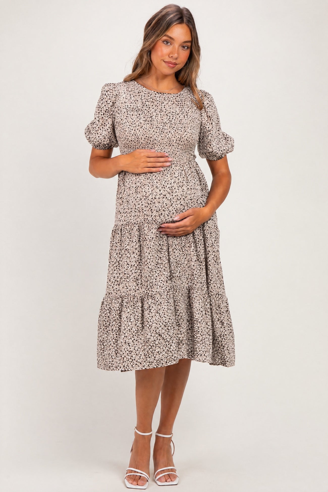 woman wearing a beige floral maternity dress with puff sleeves and tiered skirt, holding her baby bump
