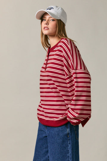 woman wearing a red and white striped oversized sweater with a round neckline and blue jeans, accessorized with a white baseball cap