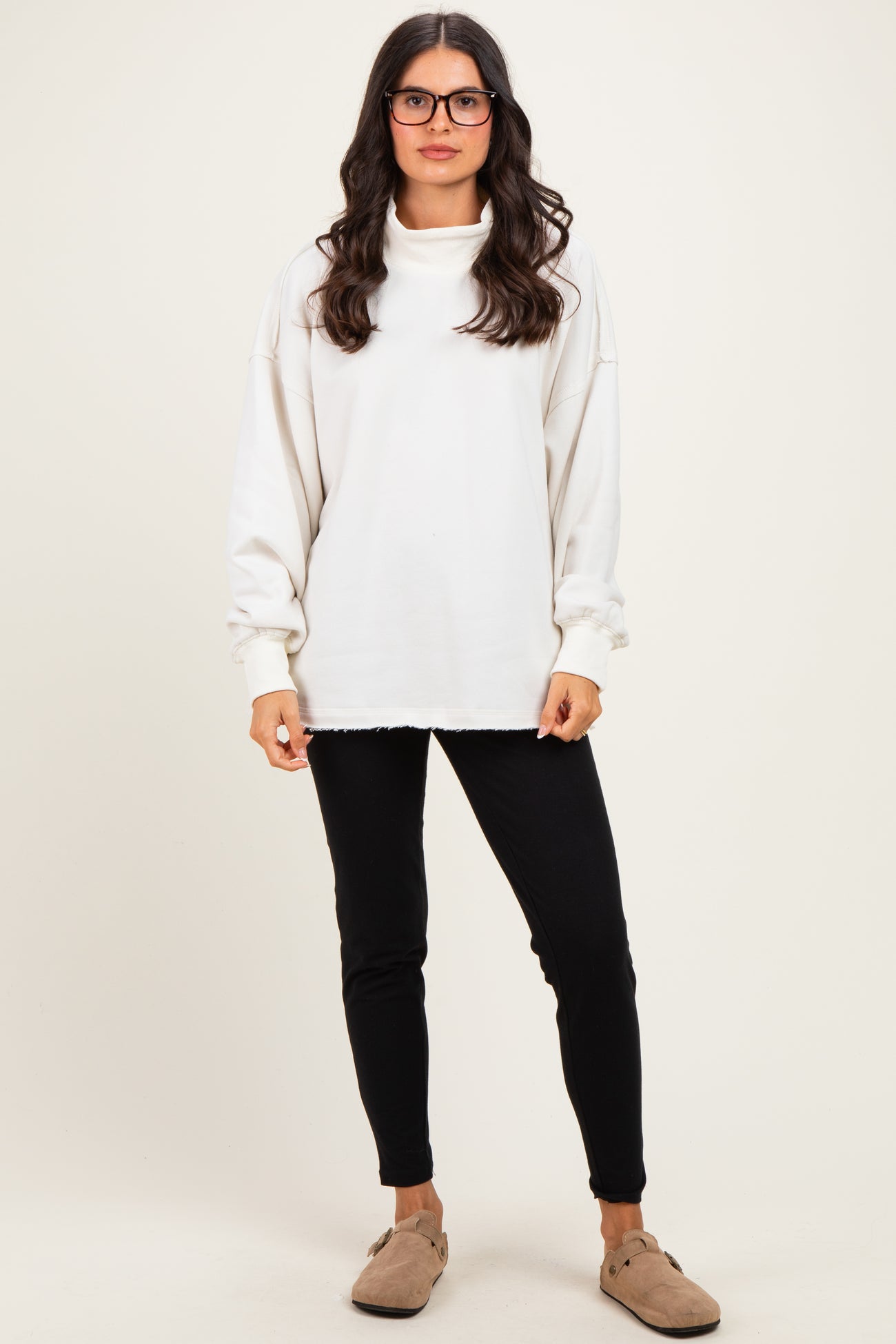 woman wearing a white oversized sweatshirt with a cowl neck and black skinny pants
