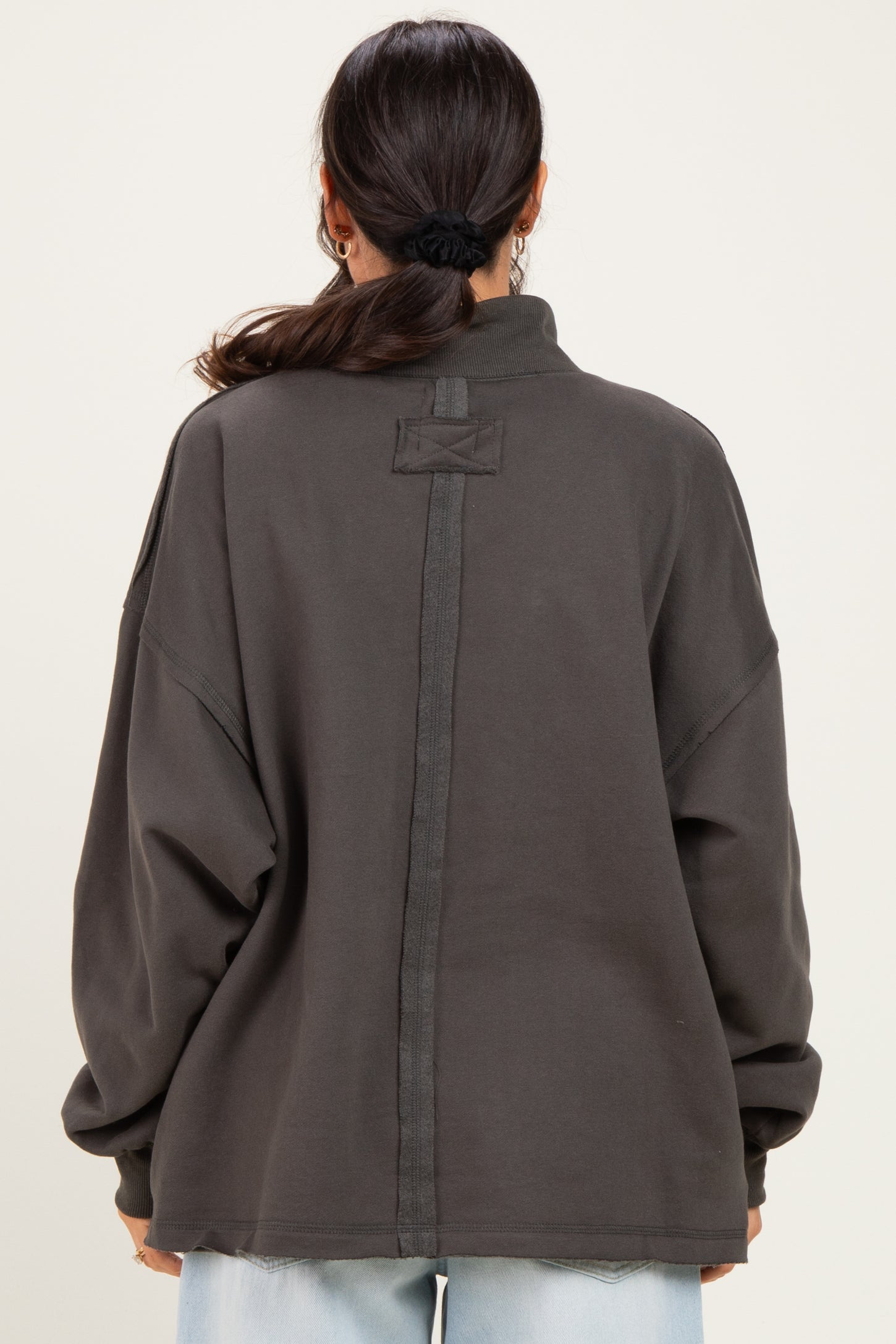 woman wearing an oversized dark gray pullover sweatshirt with a high collar and back seam detail