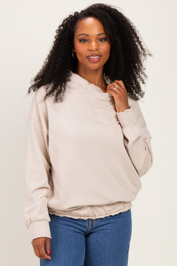 woman wearing a beige oversized sweatshirt with a gathered hem and a high neckline, styled with blue jeans