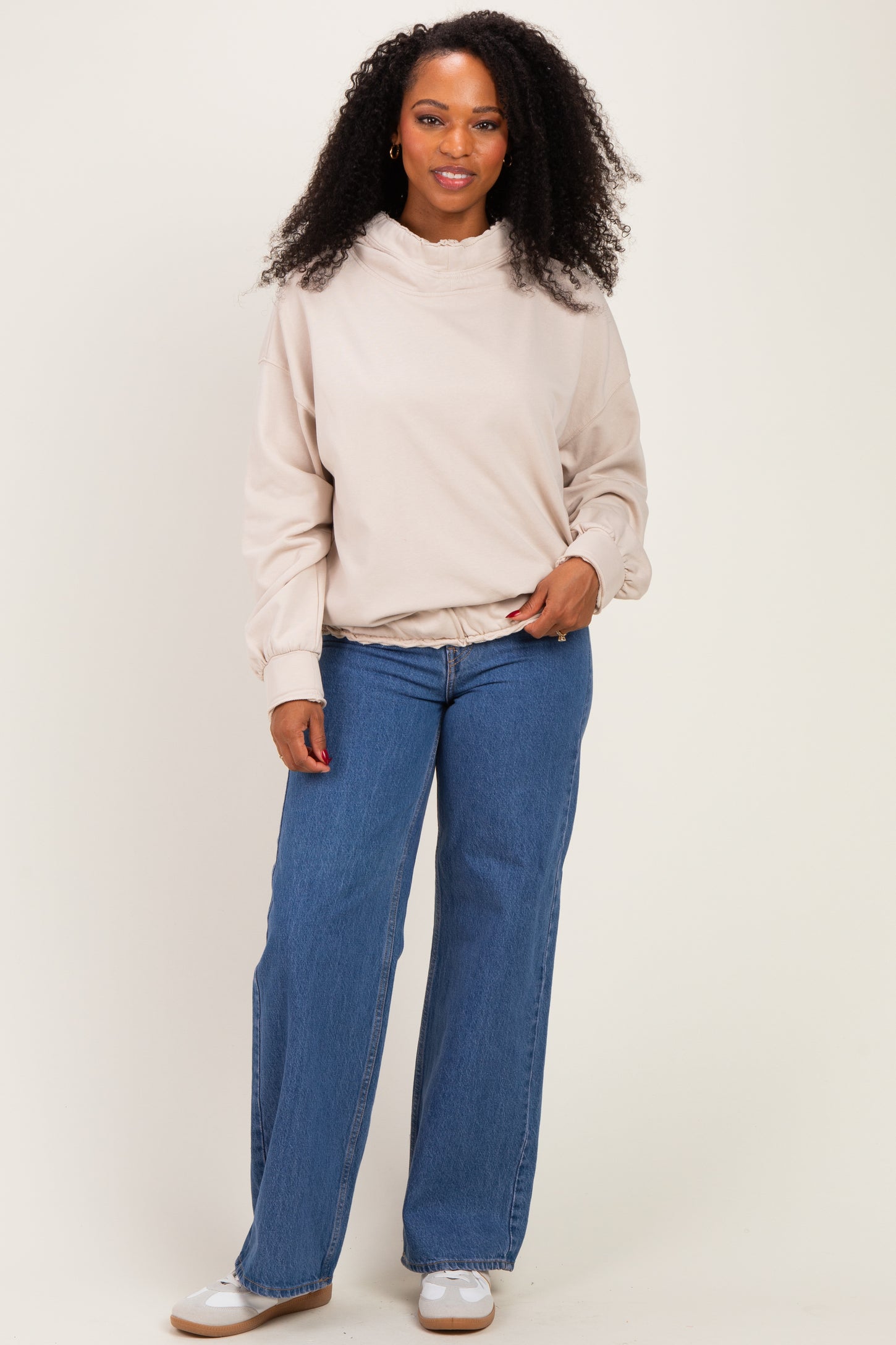 woman wearing a beige pullover sweatshirt with a ruffled collar and wide-leg blue jeans