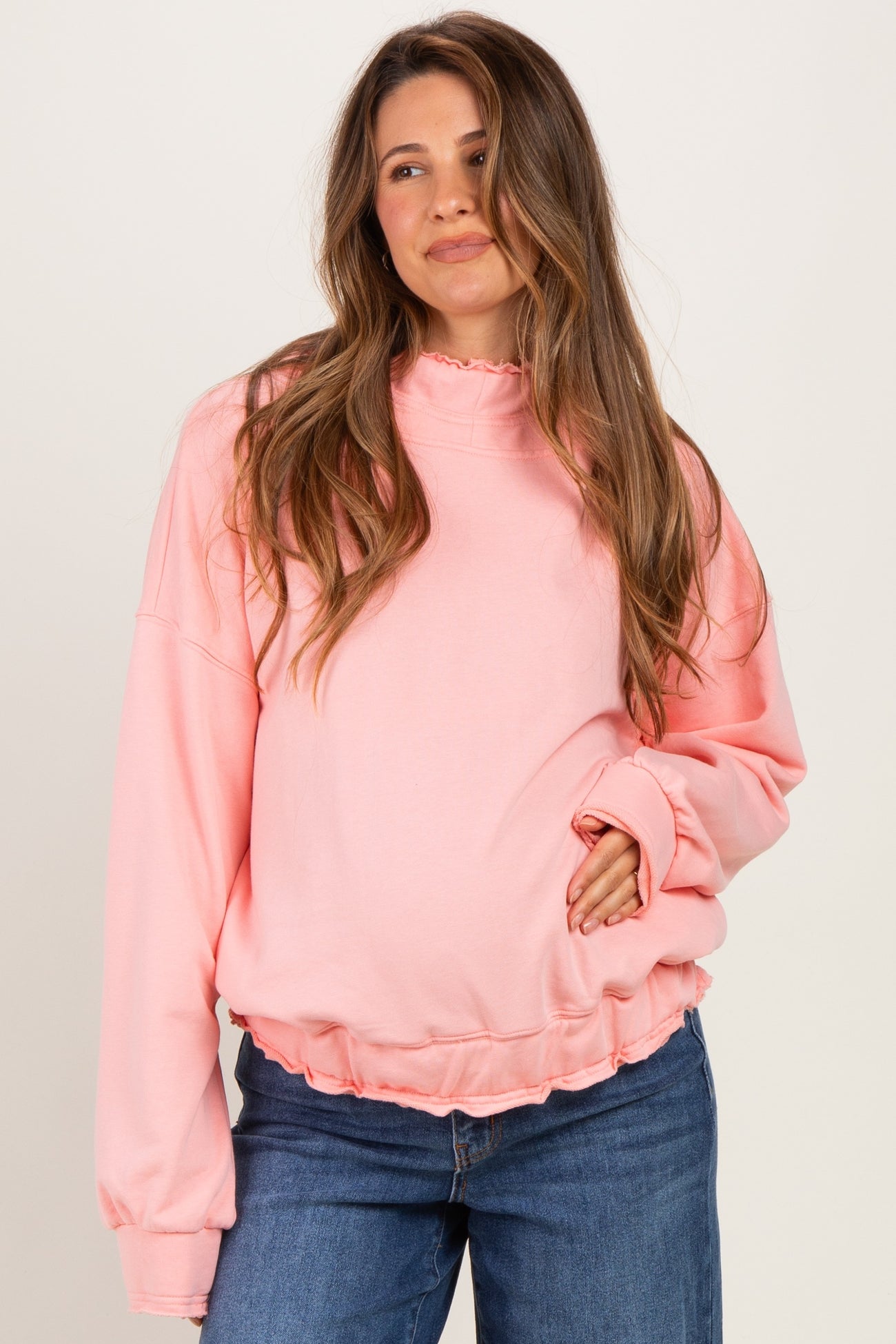 woman wearing a pink maternity sweatshirt with ruffled hem and holding her baby bump