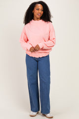 woman wearing a pink oversized sweatshirt with ruffle detailing and high-waisted blue wide-leg jeans