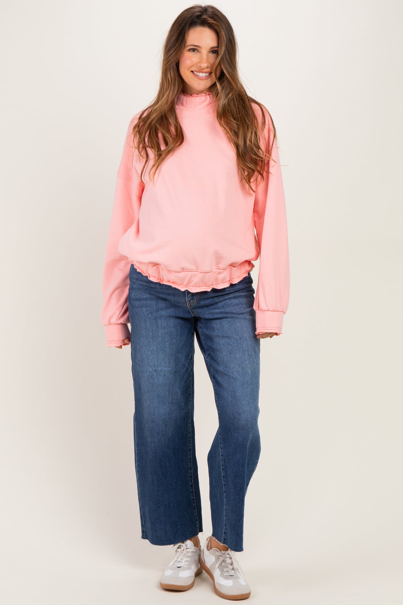 woman wearing a light pink maternity sweatshirt with a gathered hem and wide-leg denim jeans, showcasing her baby bump