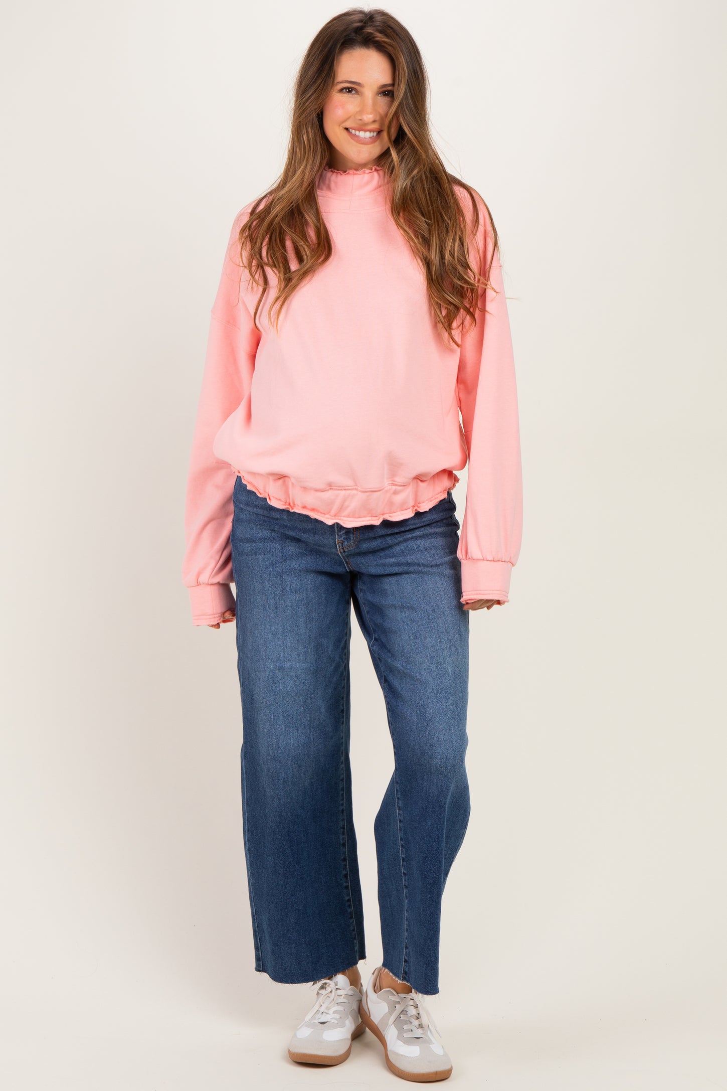 woman wearing a light pink maternity sweatshirt with a gathered hem and wide-leg denim jeans, showcasing her baby bump