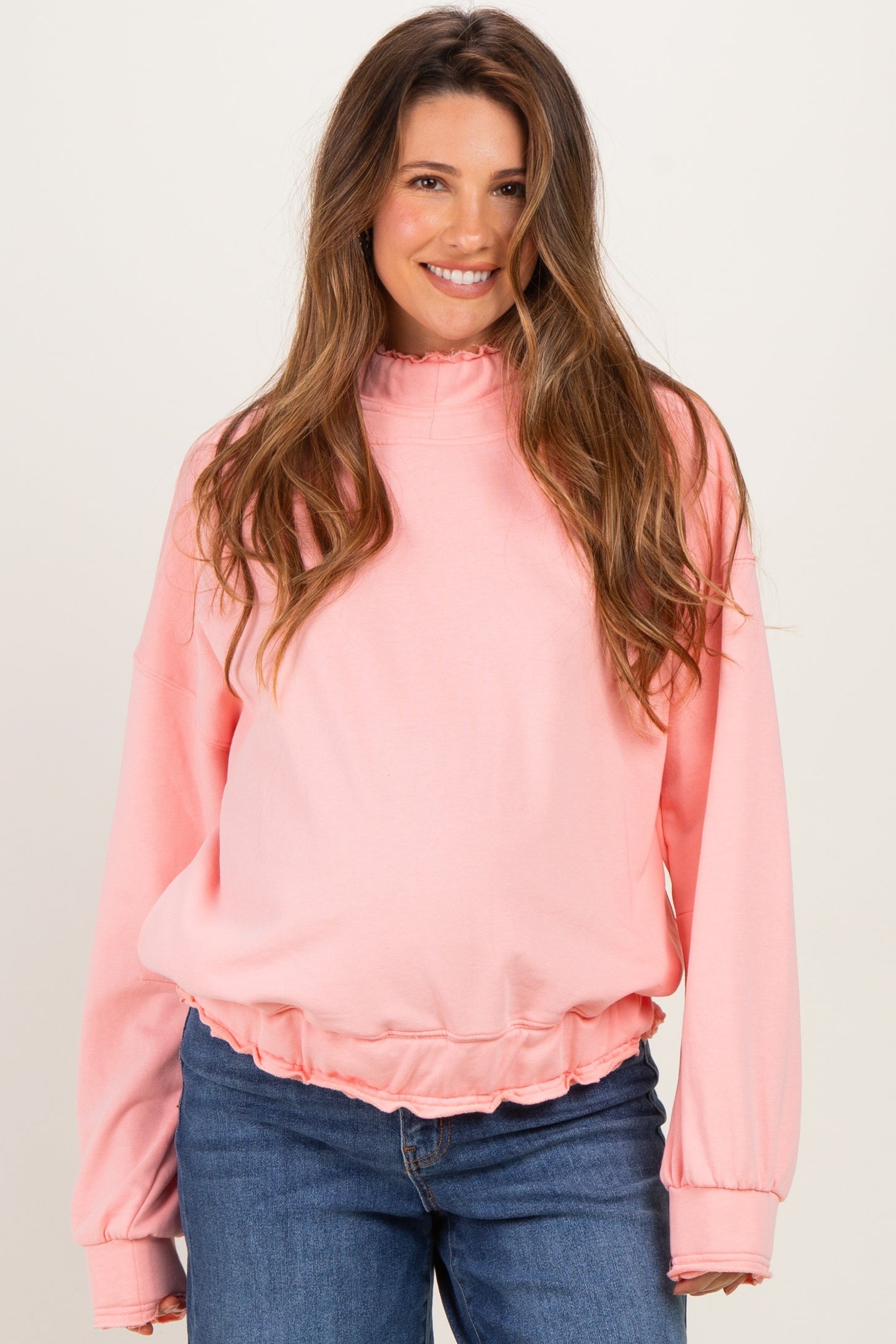 woman wearing a light pink maternity sweatshirt with a ruffled hem and long sleeves, showing her baby bump