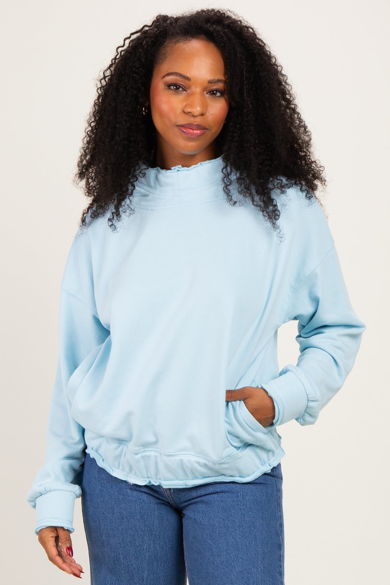 woman wearing a light blue oversized sweatshirt with a mock neck and gathered hem, styled with blue jeans