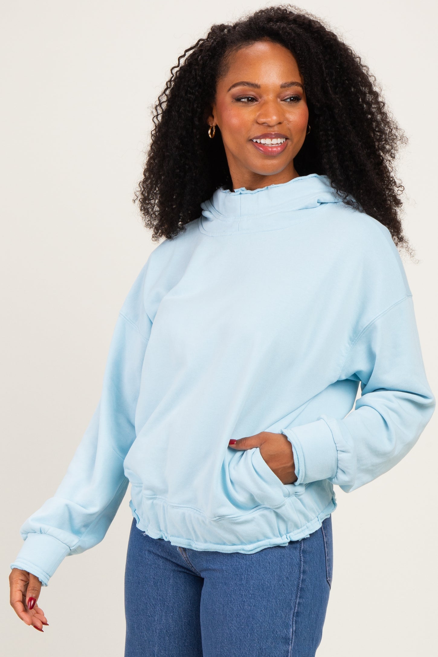 woman wearing a light blue oversized hoodie with a drawstring and front pockets, styled with high-waisted jeans