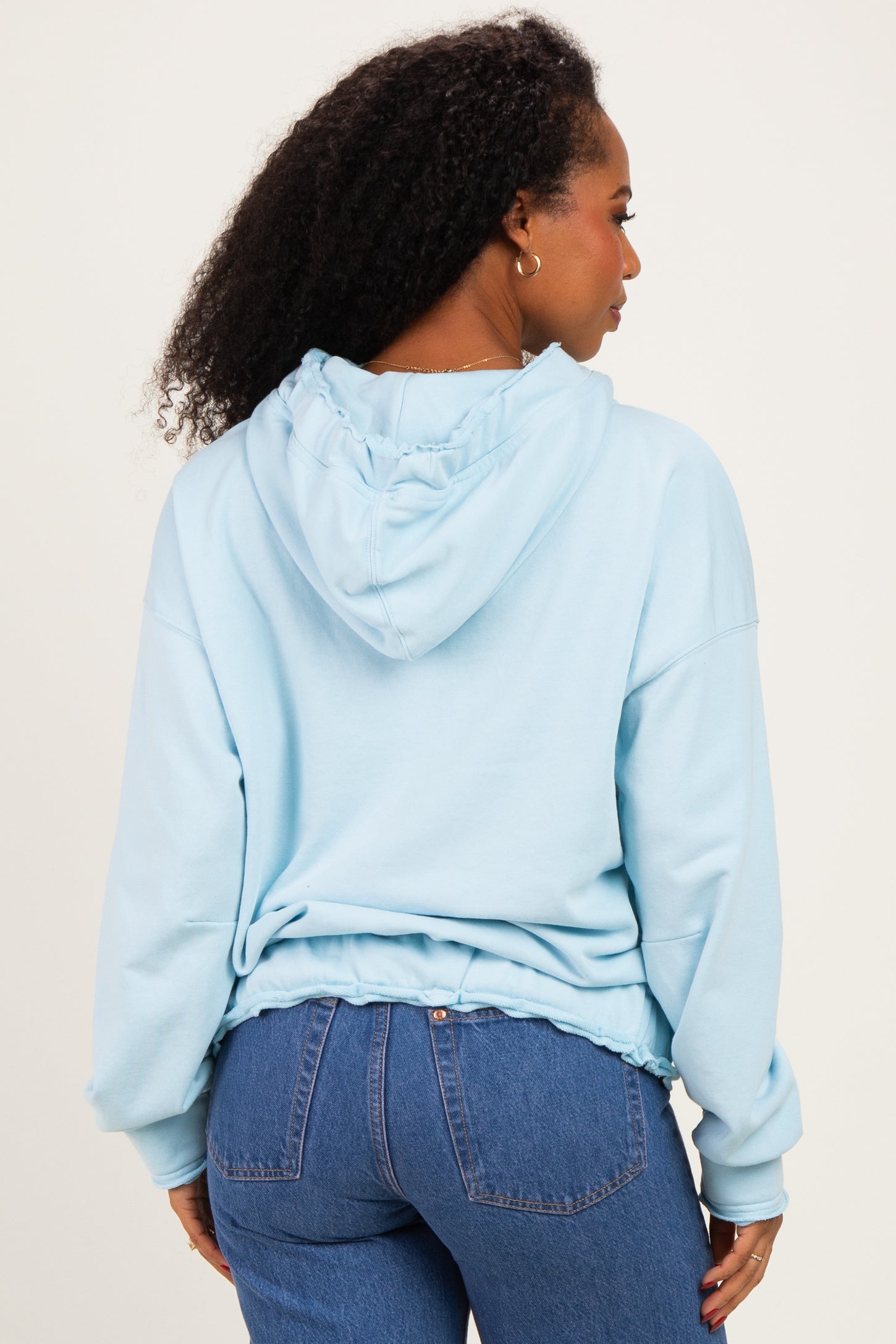 woman wearing a light blue hooded sweatshirt with a relaxed fit and ruffled hem, seen from the back