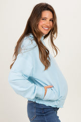 woman wearing a light blue maternity hoodie with a gathered hem and side pockets, showcasing her baby bump