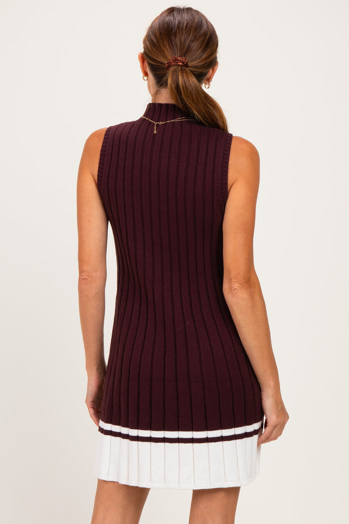 woman wearing a burgundy sleeveless ribbed sweater dress with a white pleated skirt, shown from the back