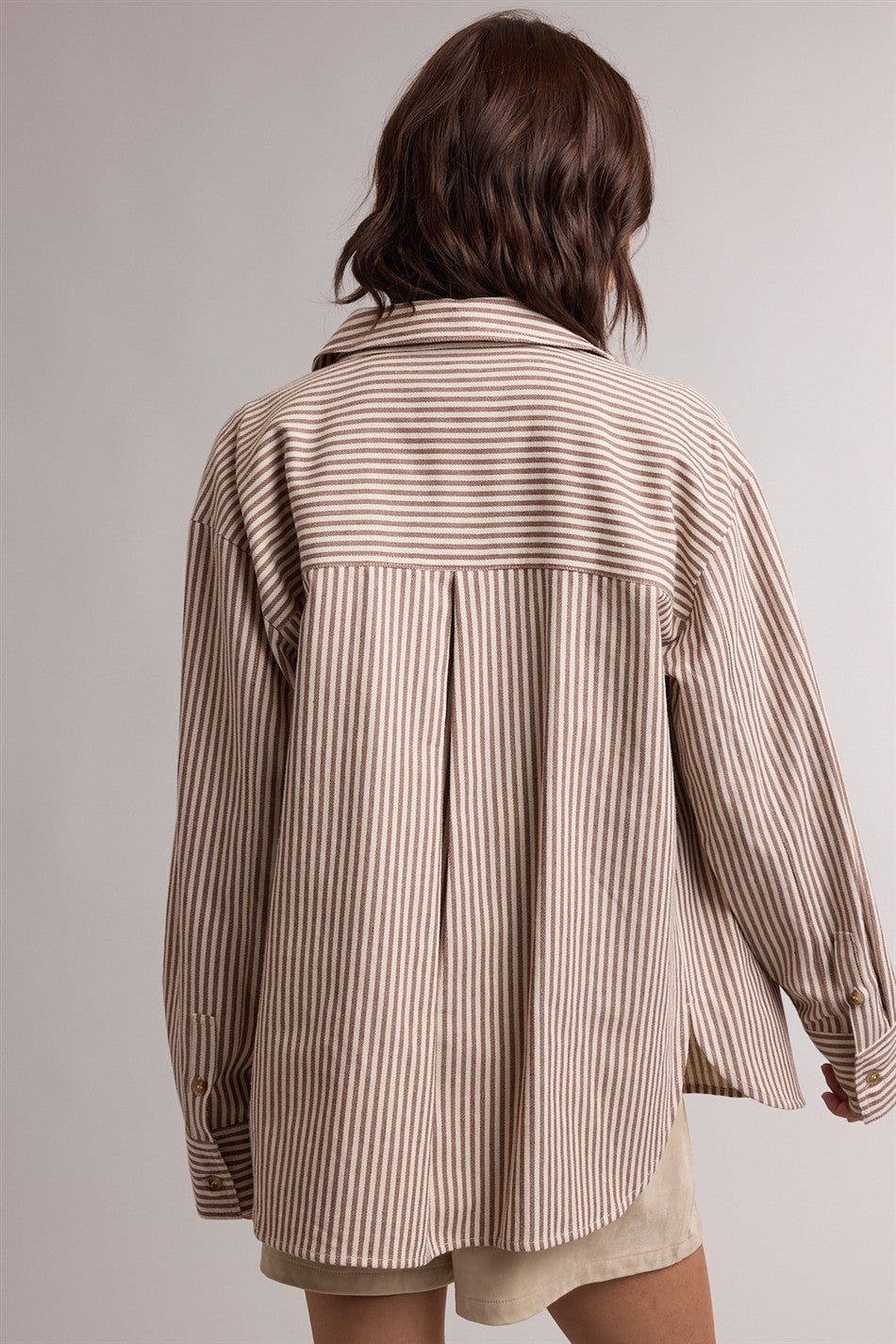 woman wearing a beige and cream striped oversized shirt with a back pleat detail