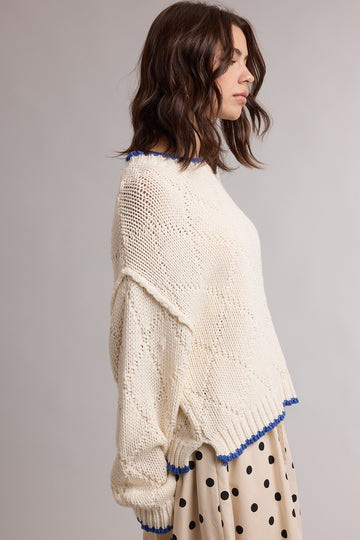 woman wearing a cream colored knitted sweater with blue trim and a loose fit, paired with a polka dot skirt