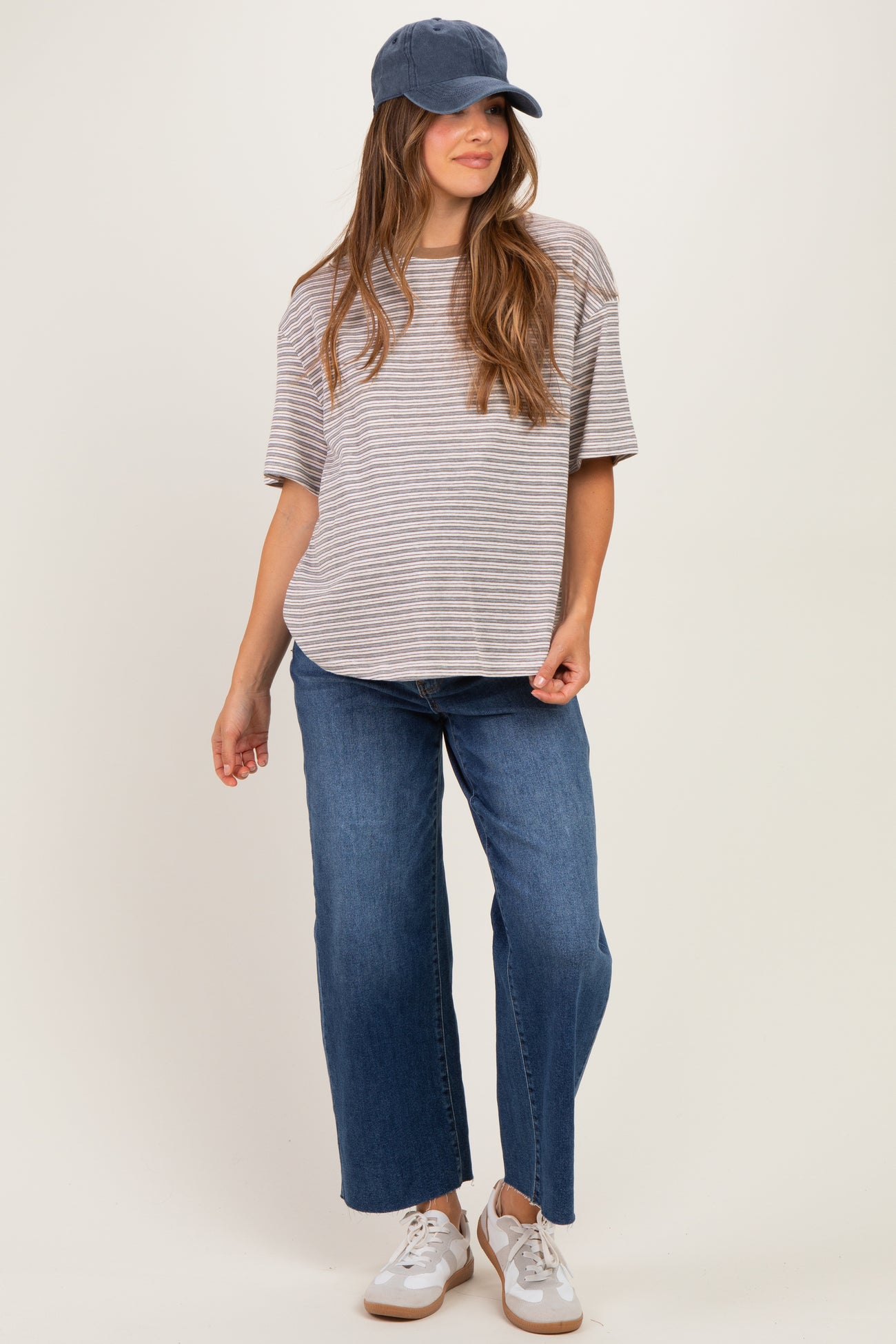 woman wearing a gray and white striped maternity t-shirt with blue wide-leg jeans and a baseball cap