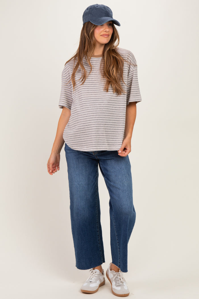 woman wearing a gray and white striped maternity t-shirt with blue wide-leg jeans and a baseball cap