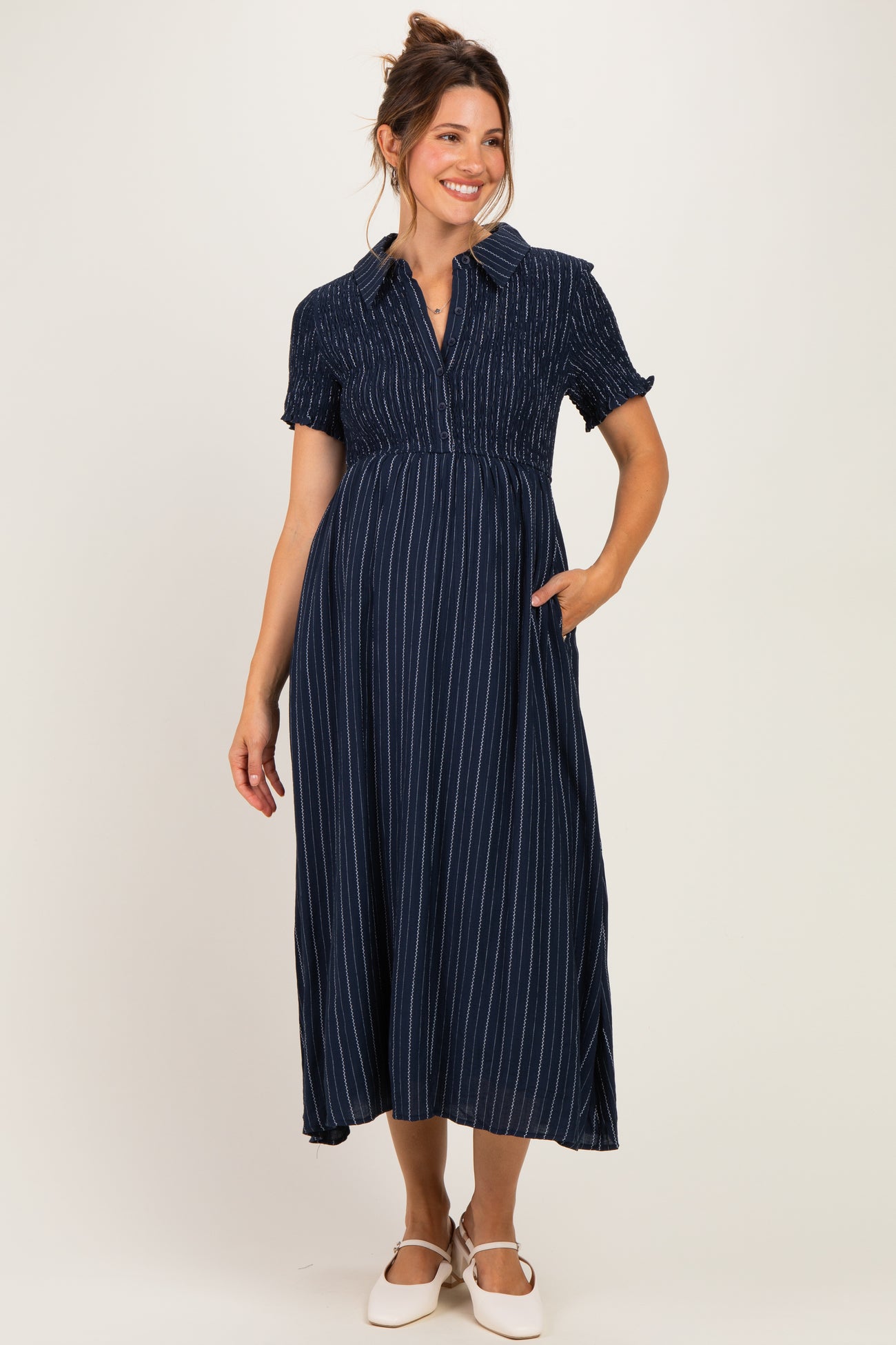 woman wearing a navy striped maternity dress with short sleeves and a collared neckline, holding her baby bump