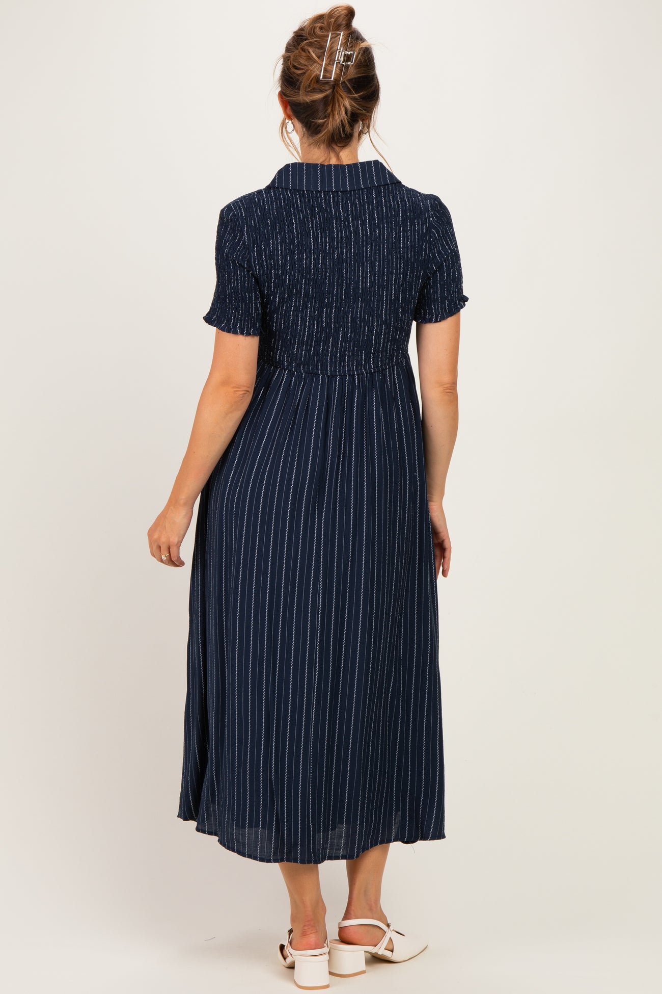 woman wearing a navy blue striped maternity dress with short sleeves and a smocked bodice, showing off her baby bump