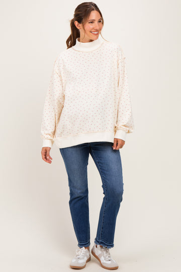 woman wearing a cream maternity sweatshirt with floral print and high collar, paired with blue maternity jeans