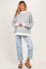 woman wearing a light gray maternity sweatshirt with floral print and white cuffs, paired with light blue distressed jeans