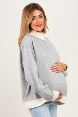 woman wearing a grey floral maternity sweatshirt with a white collar, holding her baby bump