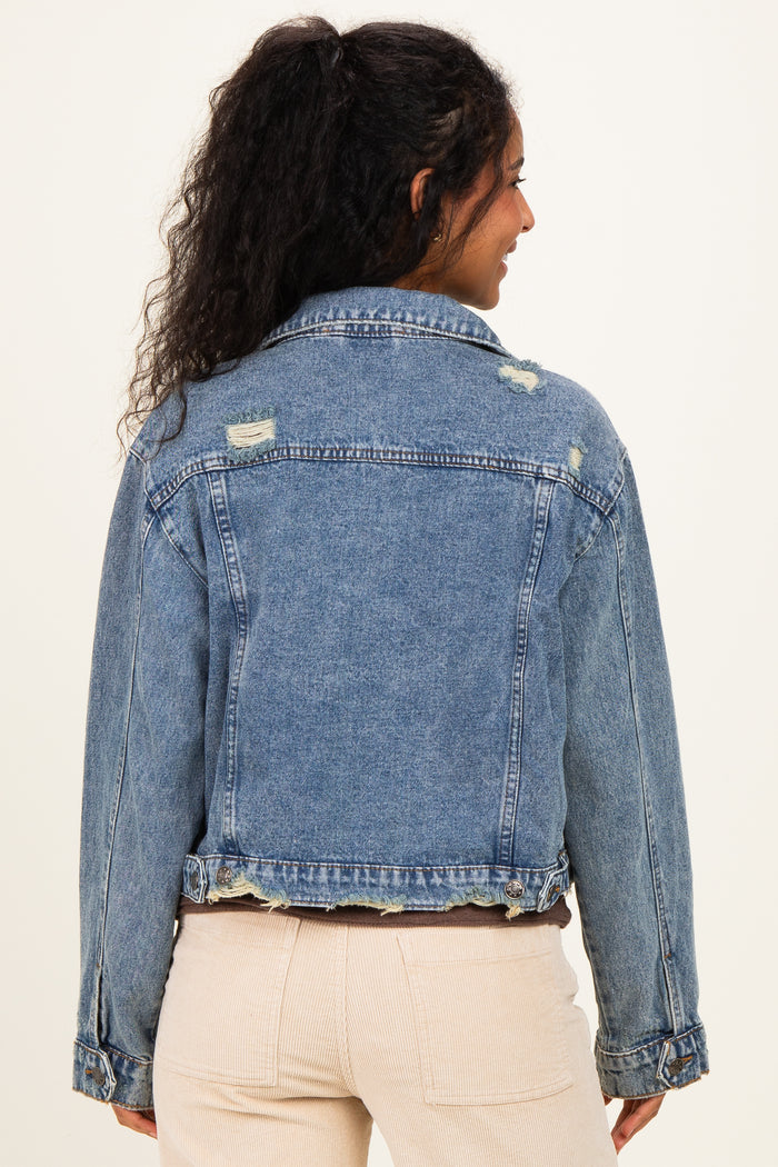 woman wearing a distressed light blue denim jacket, showcasing a relaxed fit and frayed hem, seen from the back