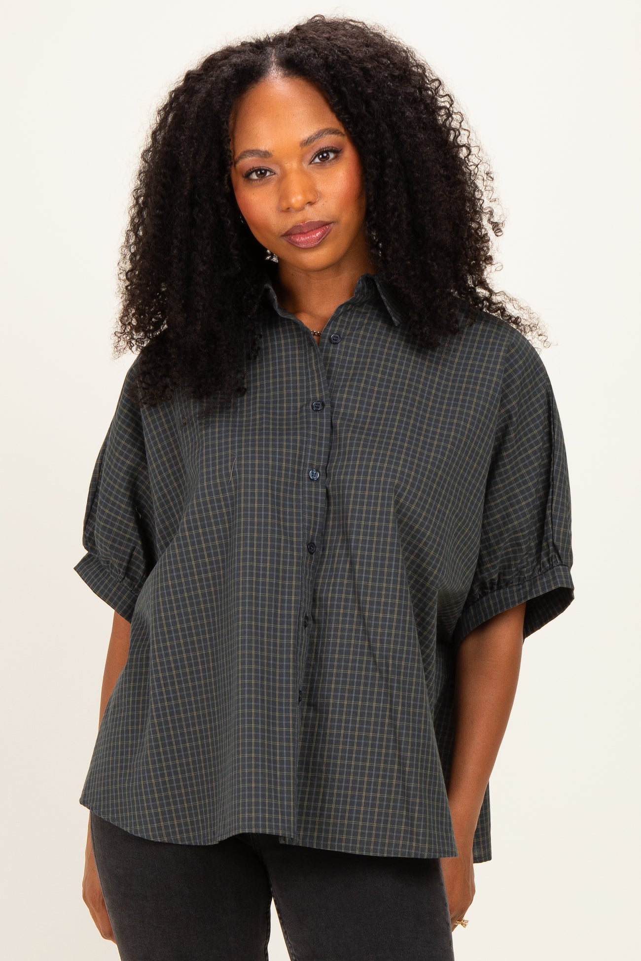 woman wearing a dark green and navy plaid oversized button-up shirt with rolled sleeves